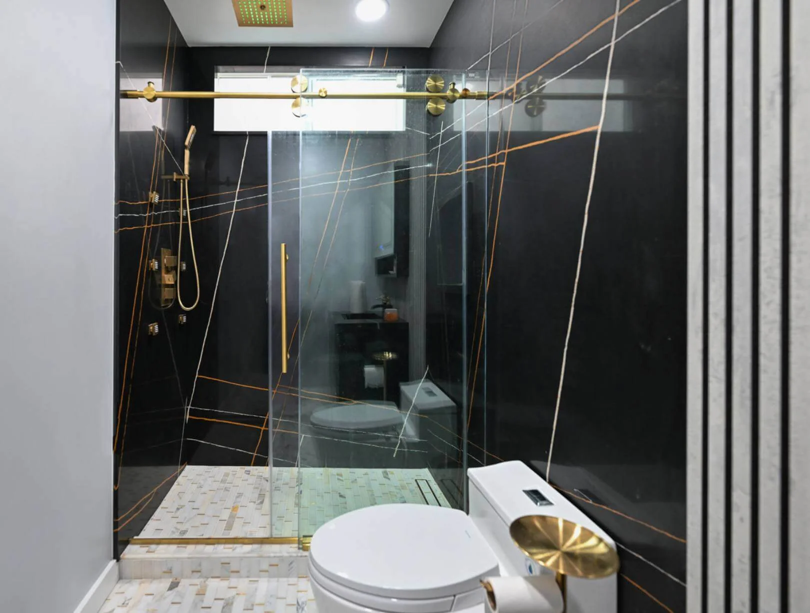 Shiny black bathroom wall with gold vertical stripes. Walk-in shower. Smart toilet.
