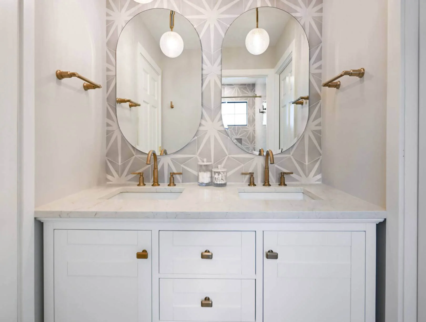 White bathroom cabinets with gray counter top. Double oblong mirrors.